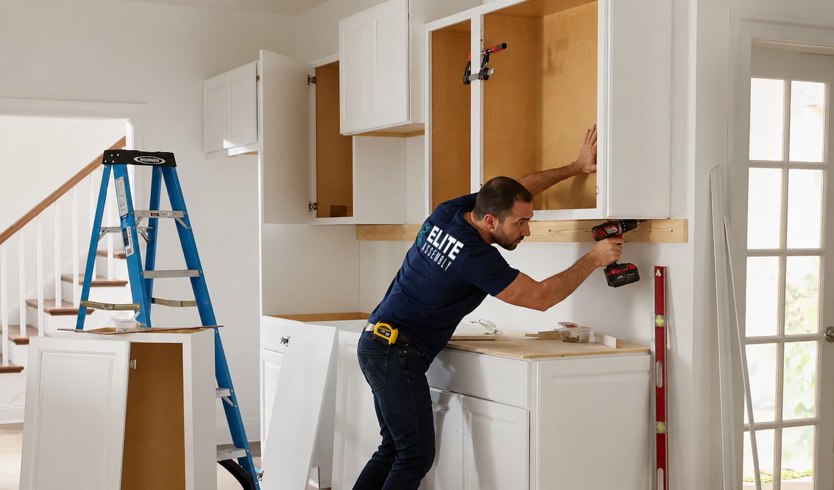 Technician installing upper kitchen cabinets with a level and drill