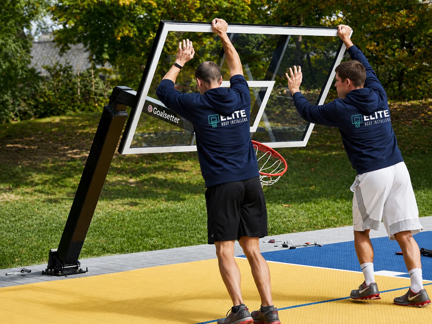 Two-person crew lifting a glass backboard into place on a newly set in-ground pole