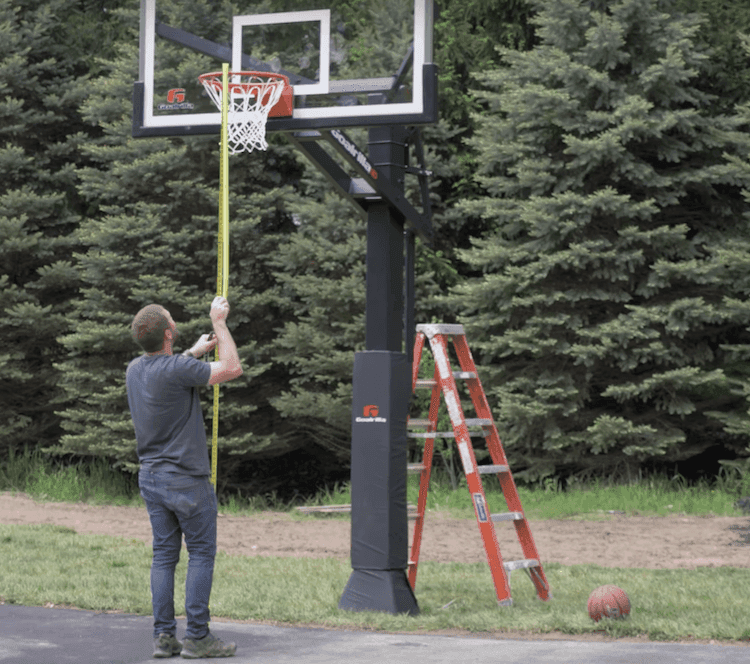 Technician measuring rim height on a newly installed basketball hoop