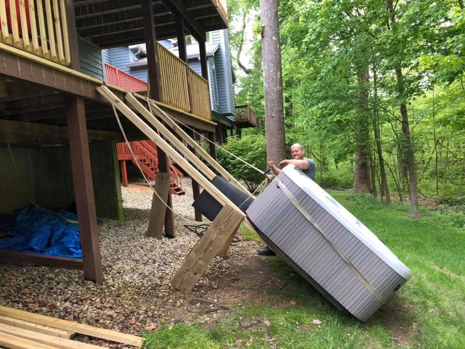 Technician lowering a hot tub down a wooden ramp under a deck