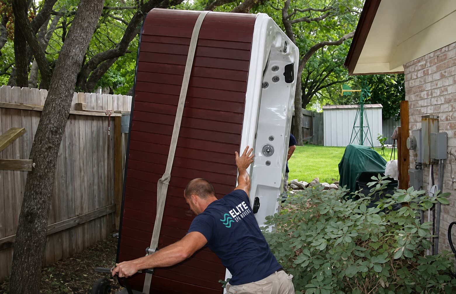 Technician moving a hot tub on a spa dolly through a backyard
